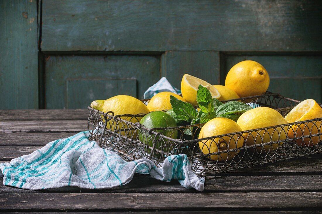 Zitronen, Limetten und frische Minze in Vintage-Drahtkorb auf Holztisch