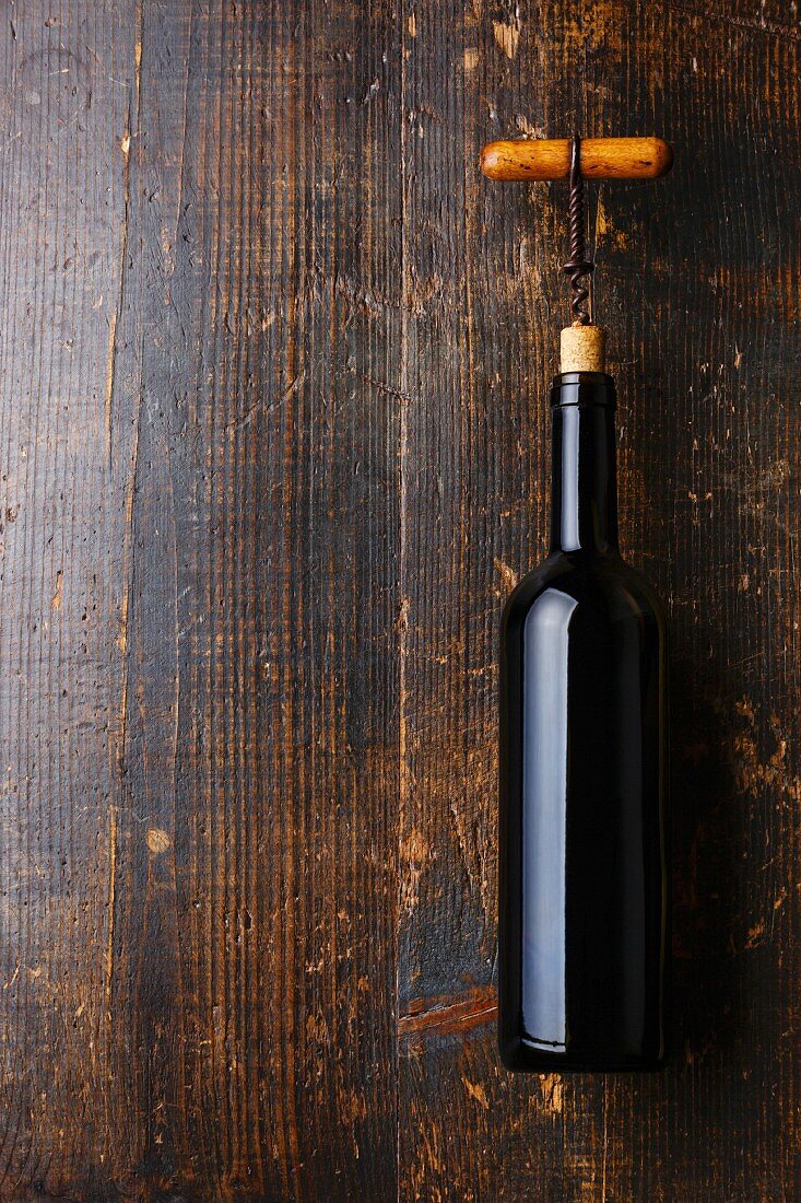 Rotweinflasche mit Korkenzieher auf Holzuntergrund