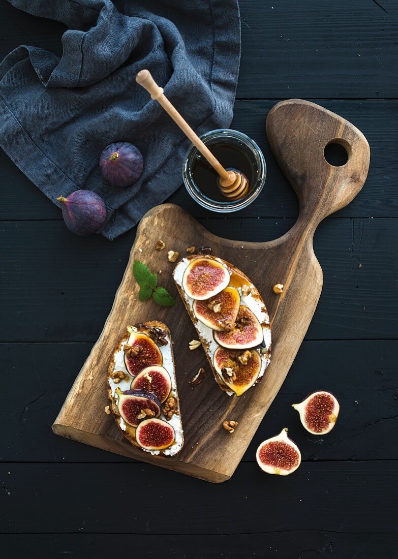 Sandwiches with ricotta, fresh figs, walnuts and honey on rustic wooden board over black backdrop