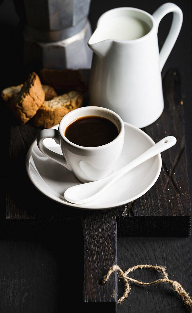 Italian coffee breakfat set: Cup of hot espresso, creamer with milk and cookies on dark wooden board