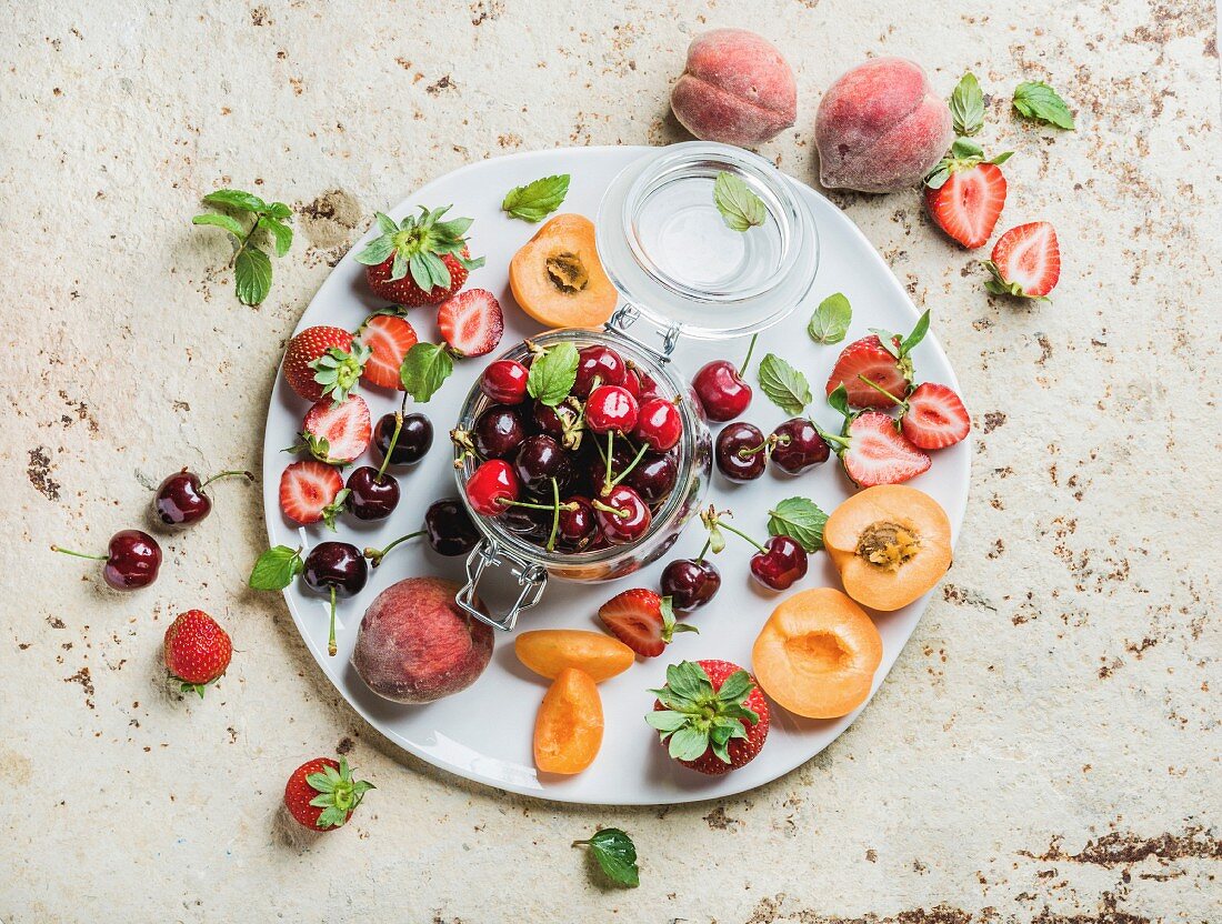 Healthy summer friut variety. Sweet cherries in glass jar, peaches, strawberries, mint leaves on white serving plate