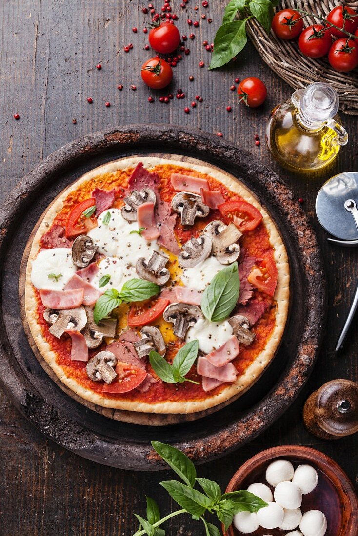 Pizza mit Schinken, Pilzen, Tomaten, Mozzarella und Basilikum