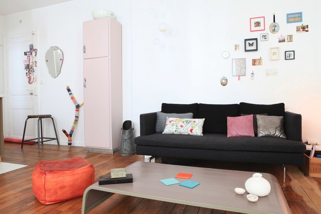 Black couch, coal scuttle, pink retro cabinet and orange pouffe in open-plan living area