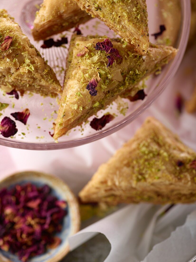 Pistachio baklava with rose petals on cake stand with pink napkin