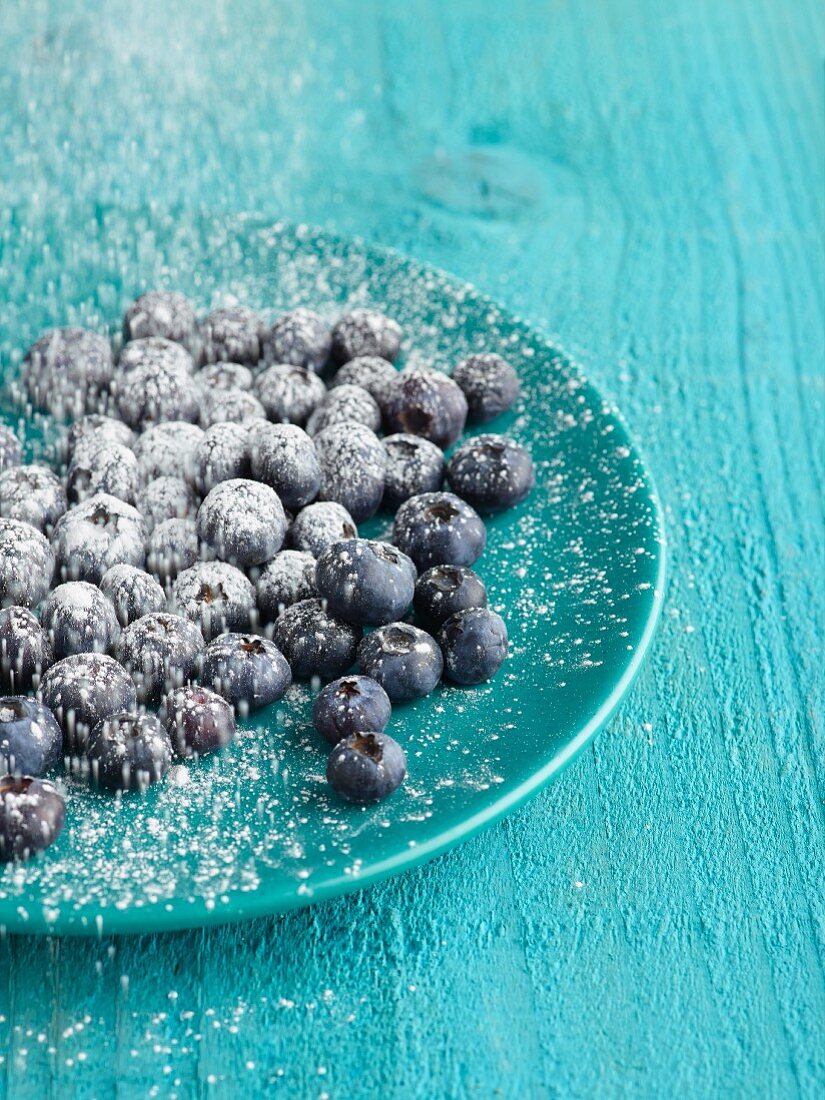 Heidelbeeren auf türkisem Teller mit Zucker bestreuen