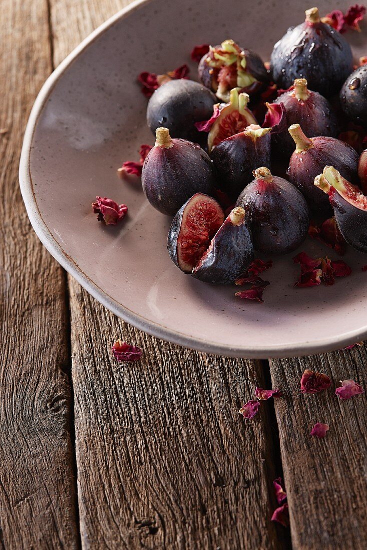 Fresh baby figs in rustic bowl on rustic table with rose petals