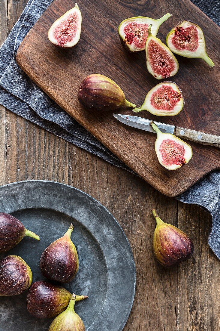 Sliced figs on a chopping board with knife and a plate of whole figs
