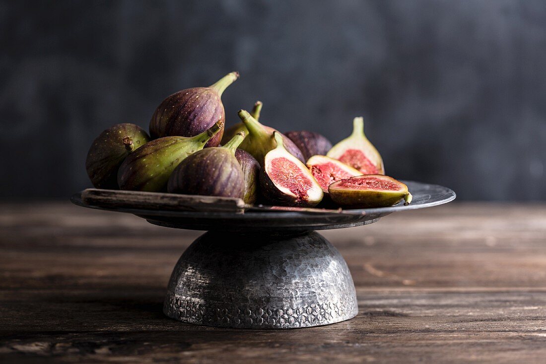 Whole and sliced figs and knife on a grey fruit stand on a wooden table