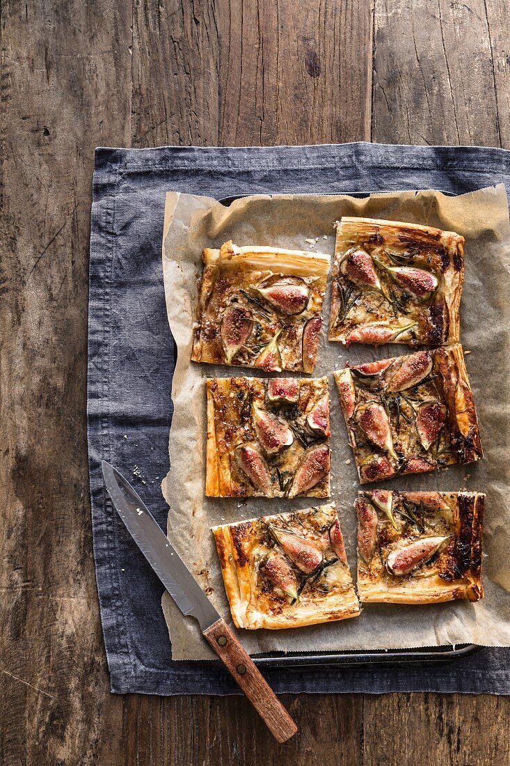 Sliced fig blue cheese and rosemary tart on baking tray with knife on grey background