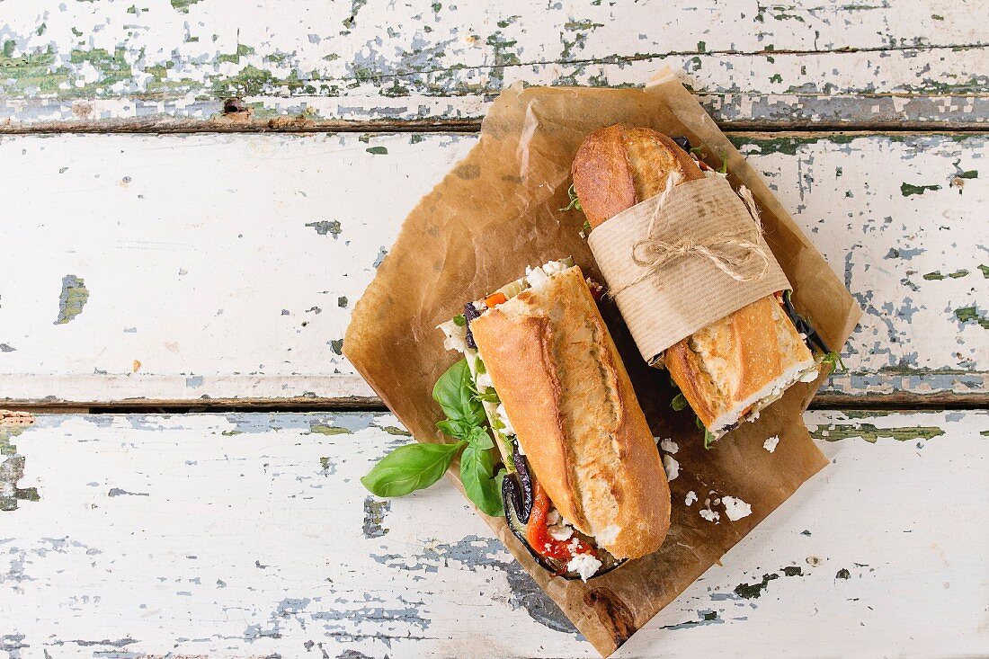 Two half of vegetarian baguette submarine sandwich with grilled eggplant, pepper and feta cheese served on baking paper