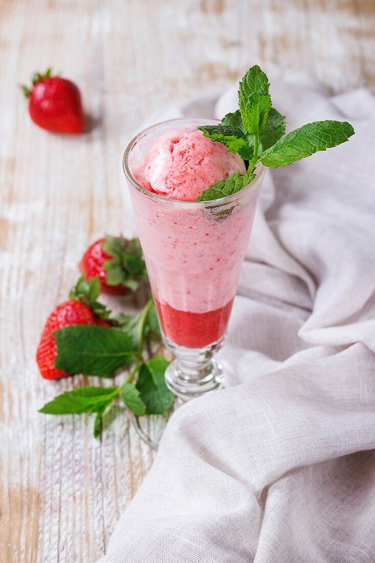 Glass of strawberry dessert with sorbet and mint, served with fresh berries over white wooden textured background