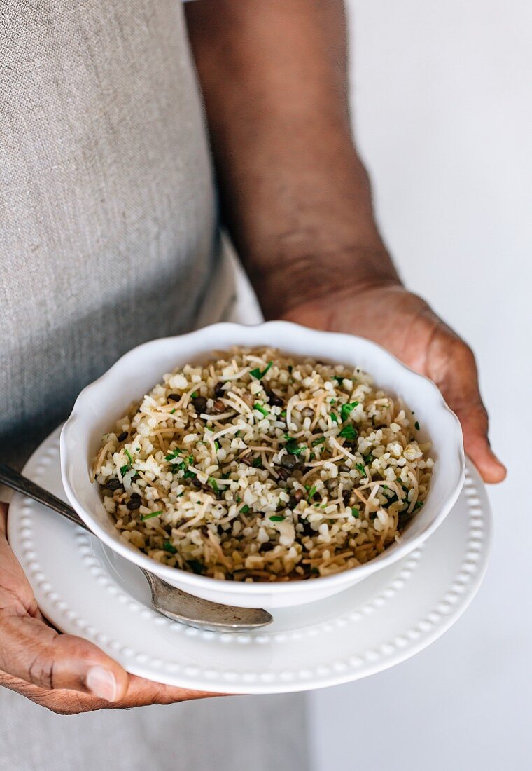 A bowl of bulgur pilaf mixed in with lentils and fresh herbs in the hands of a man