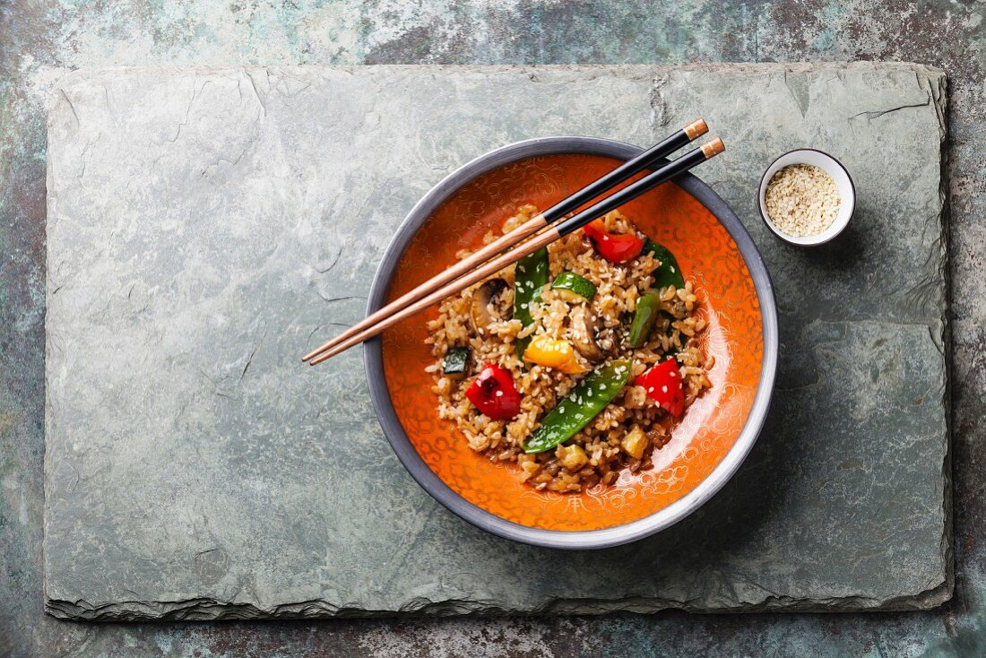 Fried Rice with vegetables in red bowl and green tea on stone slate background