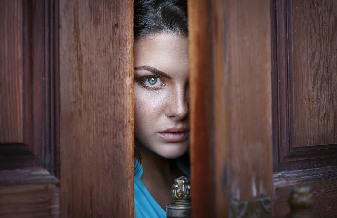 A brunette woman peeking through the crack of a door
