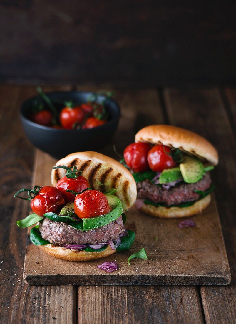 Homemade burgers with avocado and cherry tomatoes on a wooden board