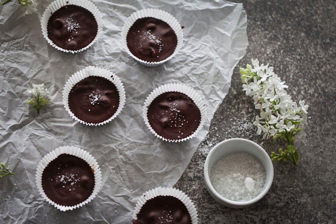 Chocolate cups filled with date caramel with sea salt on a white paper and grey background