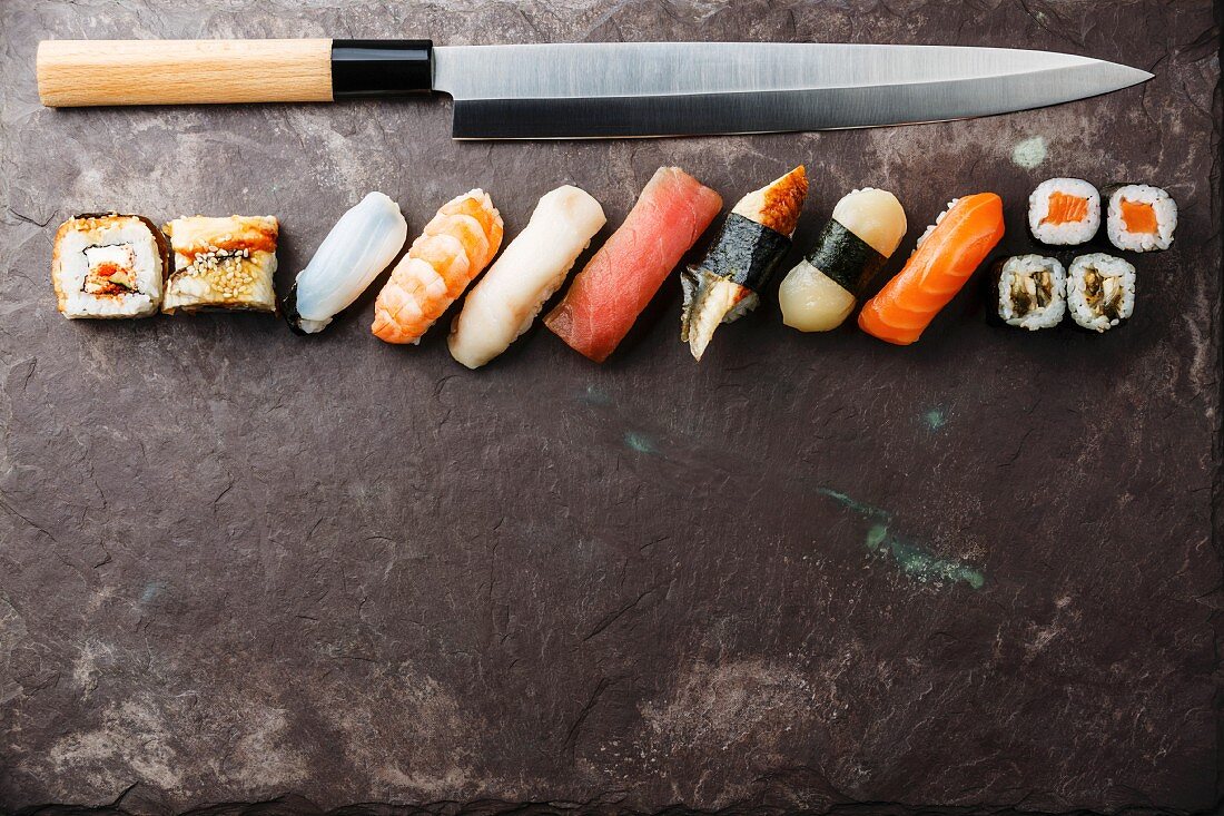 Verschiedene Sushi mit Sushi-Messer auf Schieferuntergrund