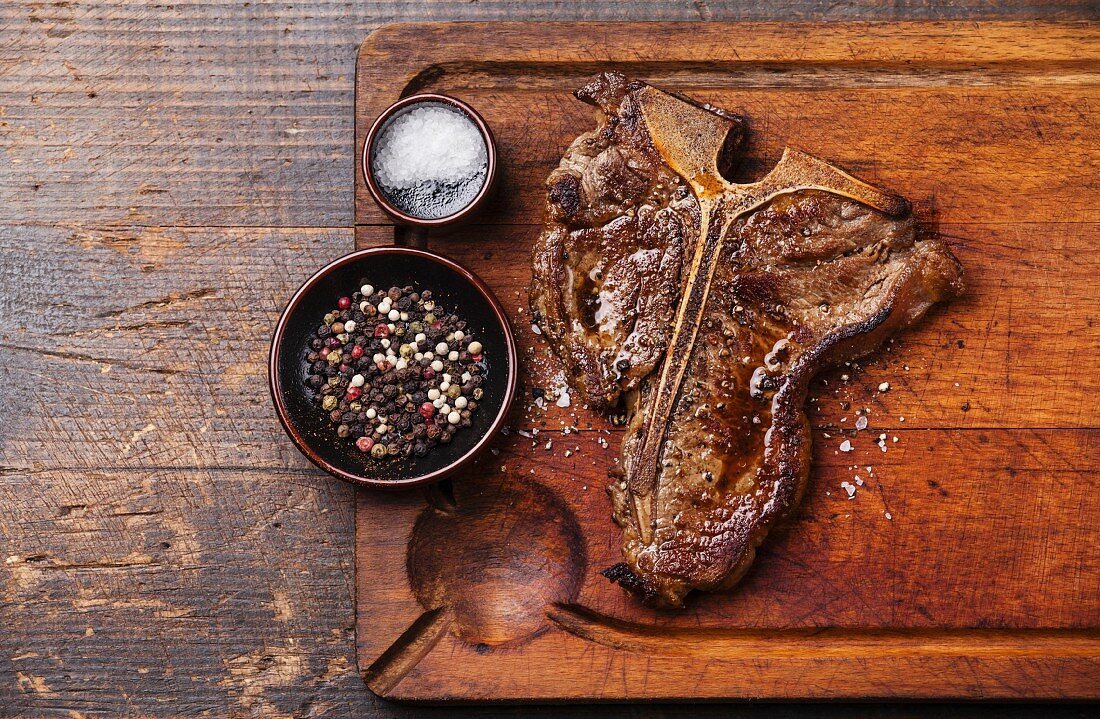 Grilled T-Bone Steak with salt and pepper on cutting board on dark wooden background