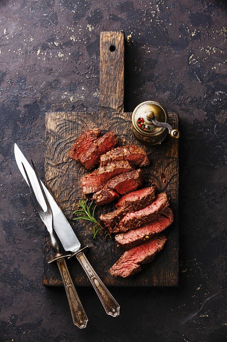 Sliced medium rare grilled Beef steak with knife and fork for meat on wooden cutting board background
