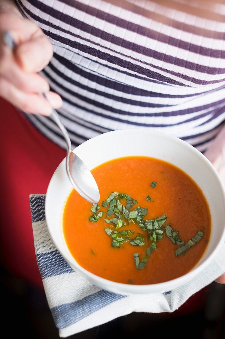 A woman with a homemade bowl of tomato and basil soup