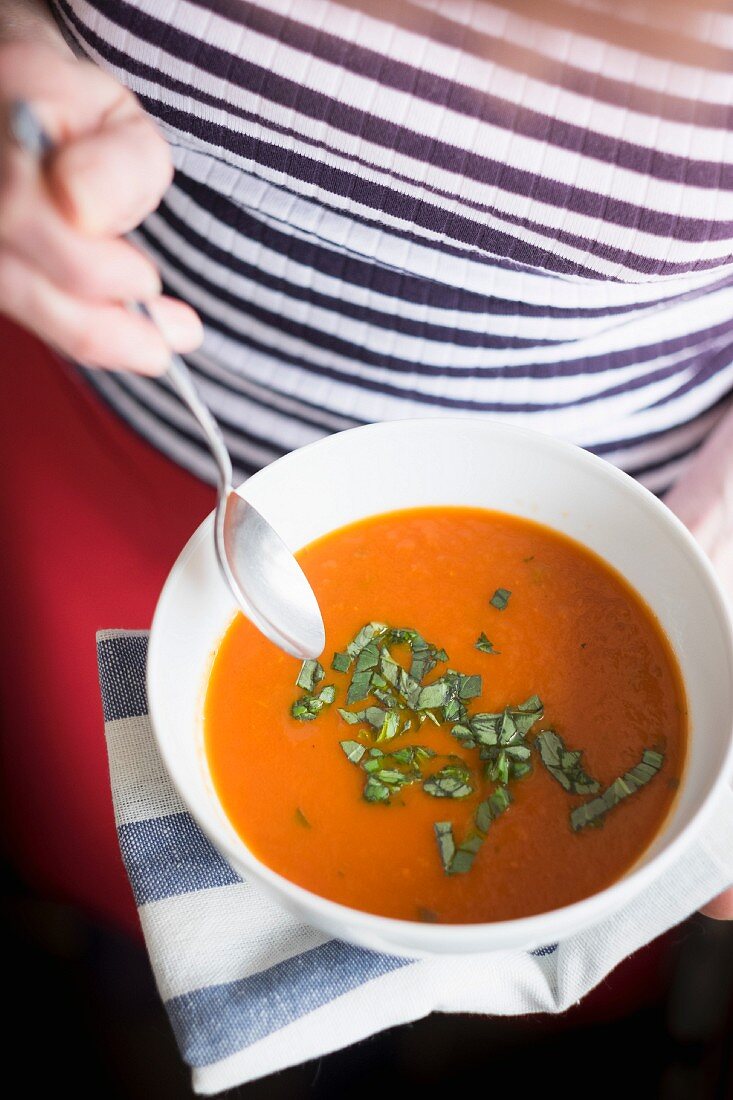 Frau isst Tomatensuppe mit Basilikum