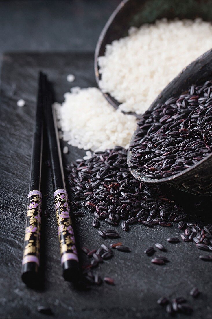 Black and white rice in old metal china bowls with black chopsticks over black slate background
