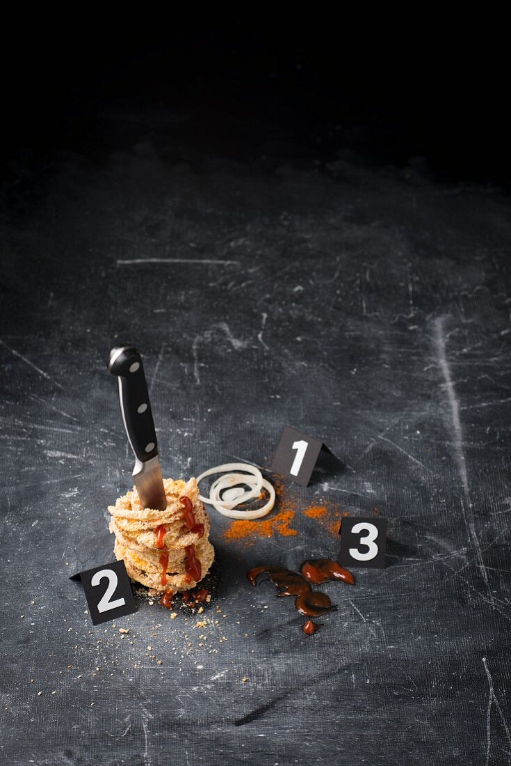 Symbolbild für eine Krimi-Szene mit Zwiebelringen, Messer und Ketchup