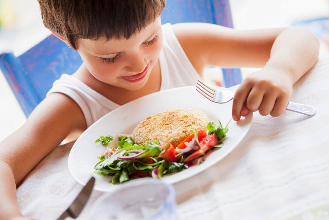 Kind isst Kichererbsenbratling mit Salat
