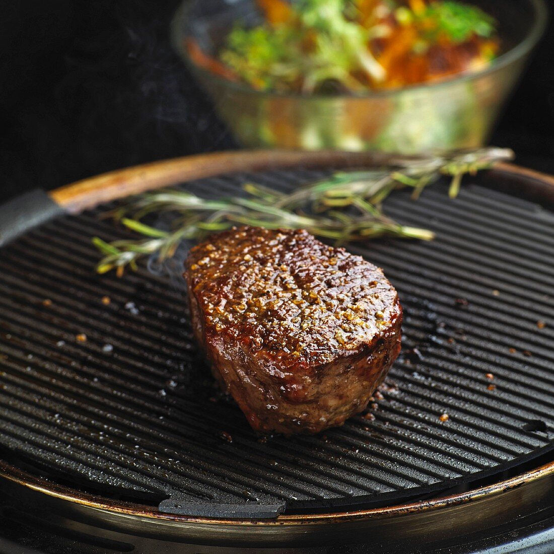 Beef fillet steak on a grill in front of a salad bowl