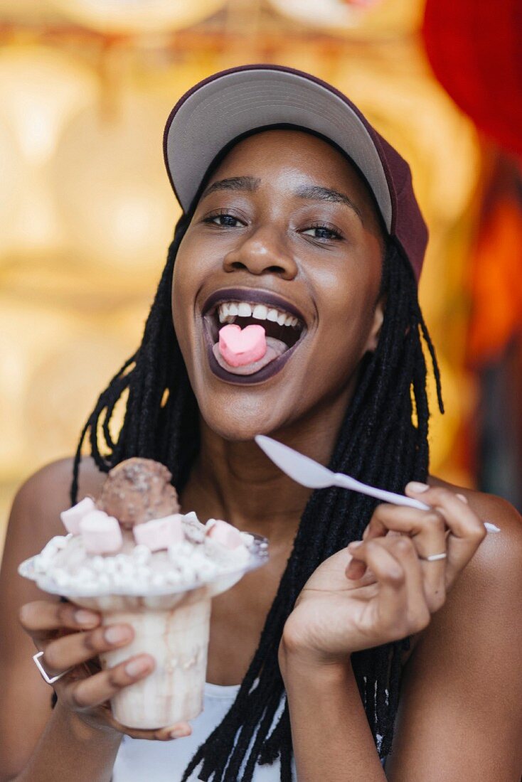 A woman with a heart-shaped candy on her tongue and an ice cream sundae in her hand