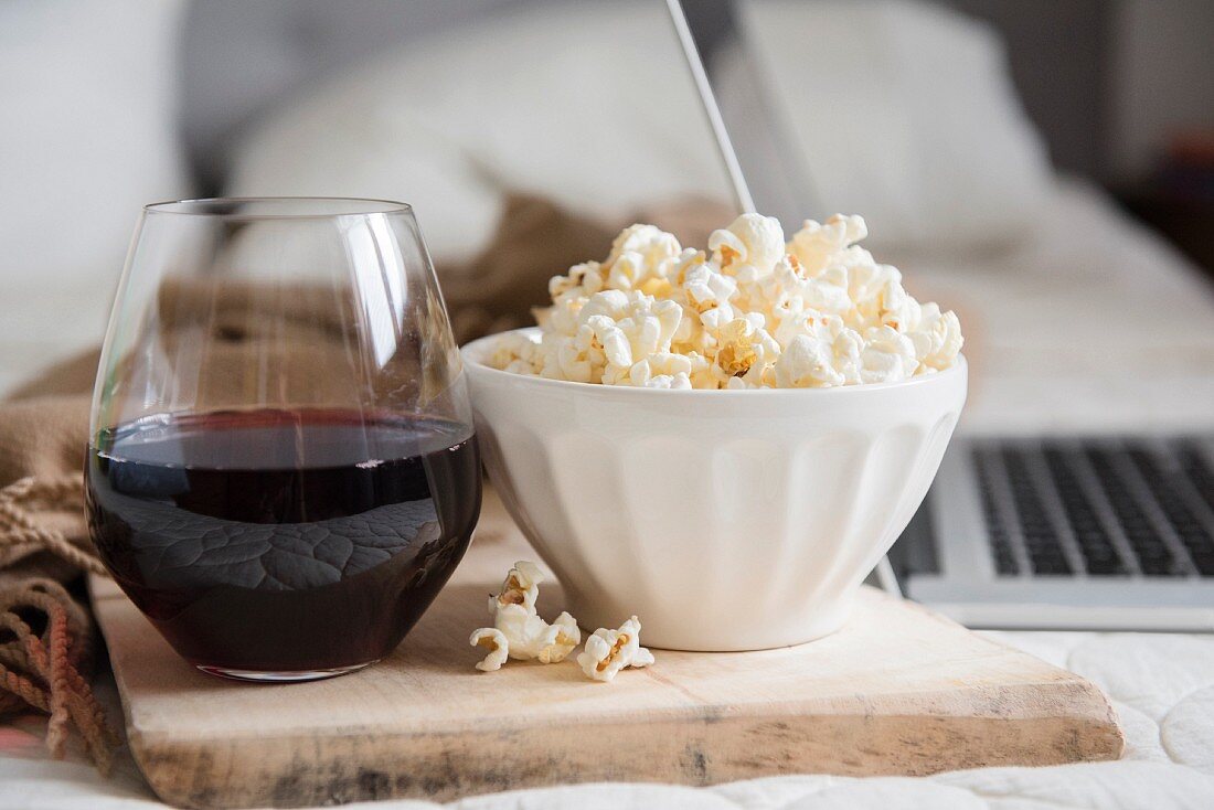 A bowl of popcorn and a glass of red wine near a laptop