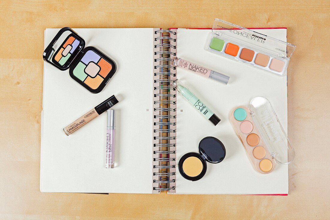 Various cosmetic products for colour-correcting laid out on a spiral-bound notebook