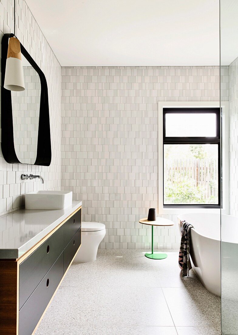 Bathroom with light textured tiles on the wall, vanity unit and free-standing bathtub