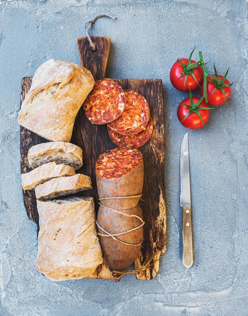 Brot und Salami auf rustikalem Holzbrett (Aufsicht)