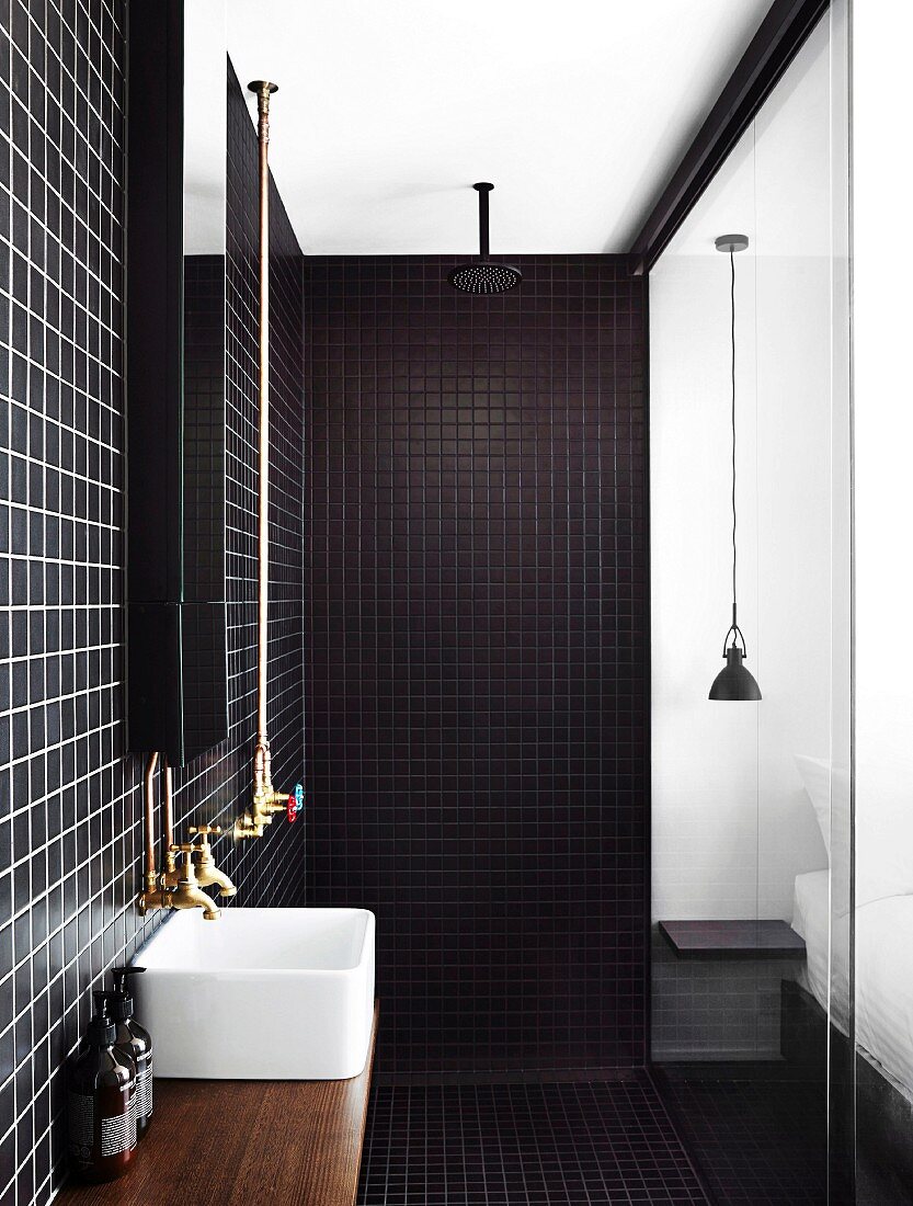 Modern shower area with dark wall and floor tiles, countertop basin and glass partition to the bedroom