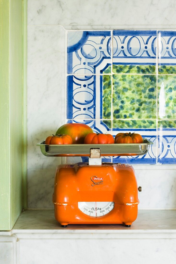 Orangefarbene Küchenwaage mit Tomaten auf Marmorsims in einer Küche