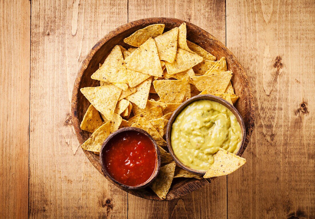 Fresh salsa and guacamole dips with nachos chips on wooden background