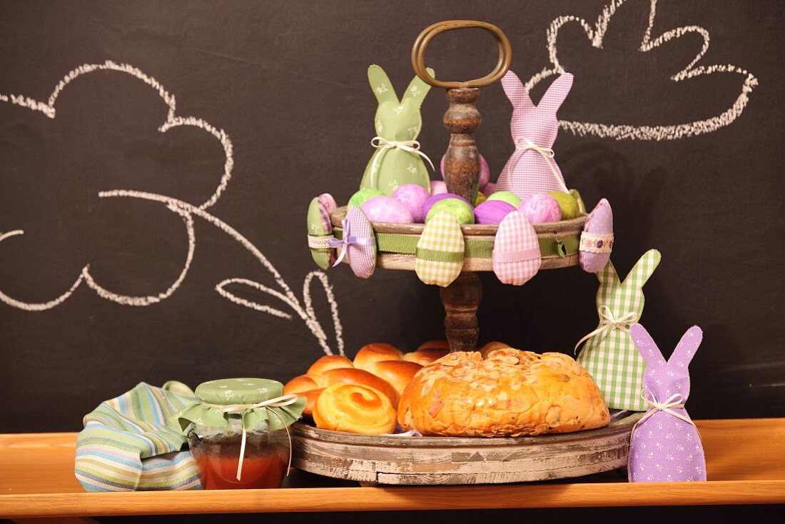 Pastries and pink and lilac Easter ornaments on cake stand against chalkboard wall