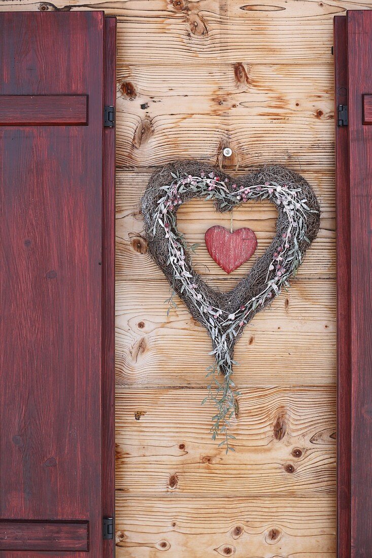 Herzkranz an Holzfassade zwischen Fensterläden