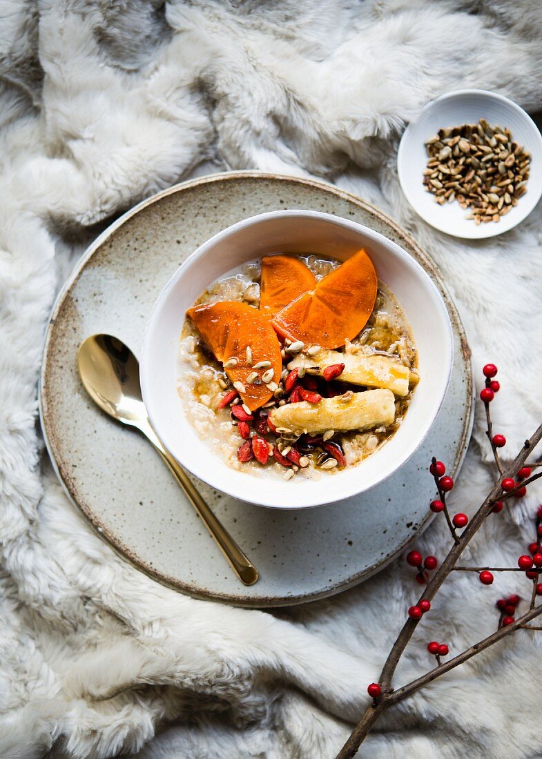 Wholegrain porridge with chai spices and topped with persimmon, banana, goji berries and sunflower seeds