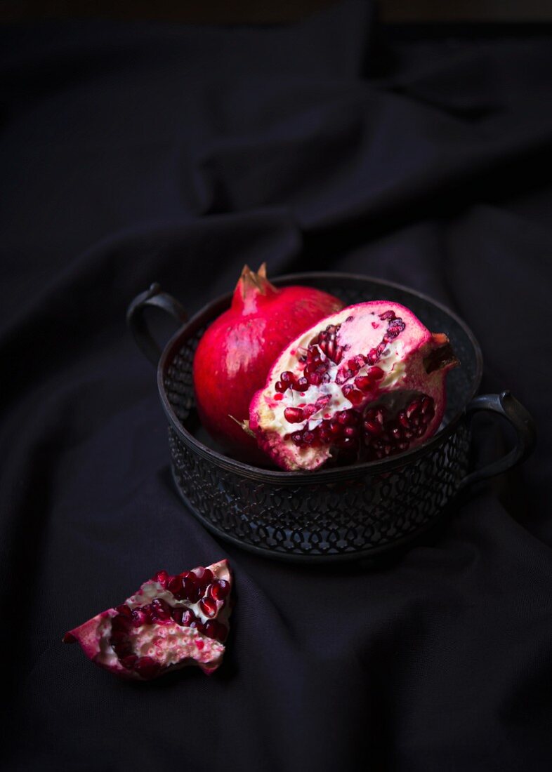 Two pomegranates in a metal bowl, one whole and one cut open
