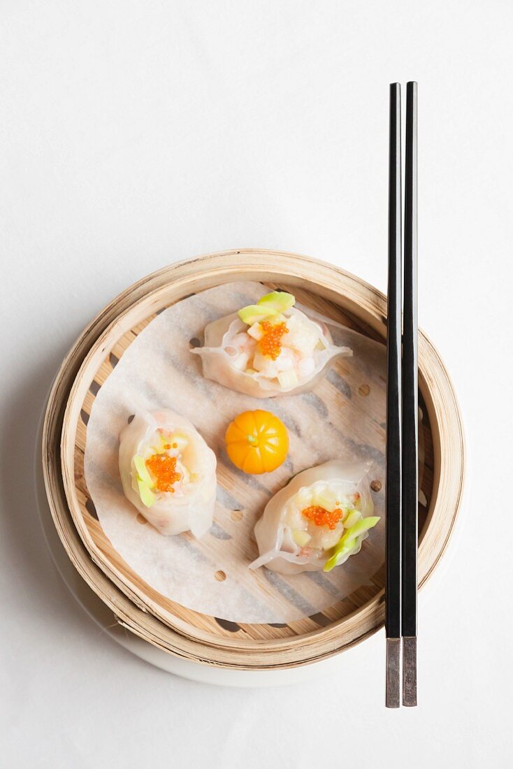Steamed Chinese dumplings with prawns and fish roe in bamboo steaming basket with chopsticks