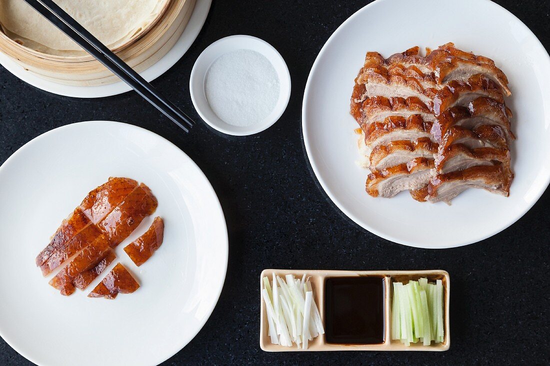 Slices of crispy Peking duck and duck skin with pancakes spring onions cucumber and hoisin sauce
