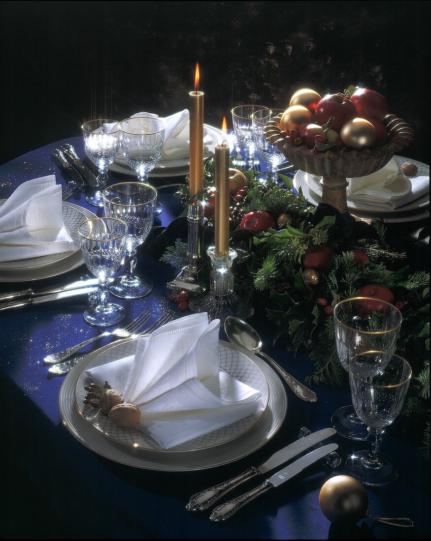 Weihnachtlich gedeckter Tisch mit Kerzen, Tannengrün & Äpfeln