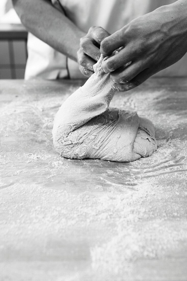 Bread being made: A baker folding the dough on a worktop dusted with flour