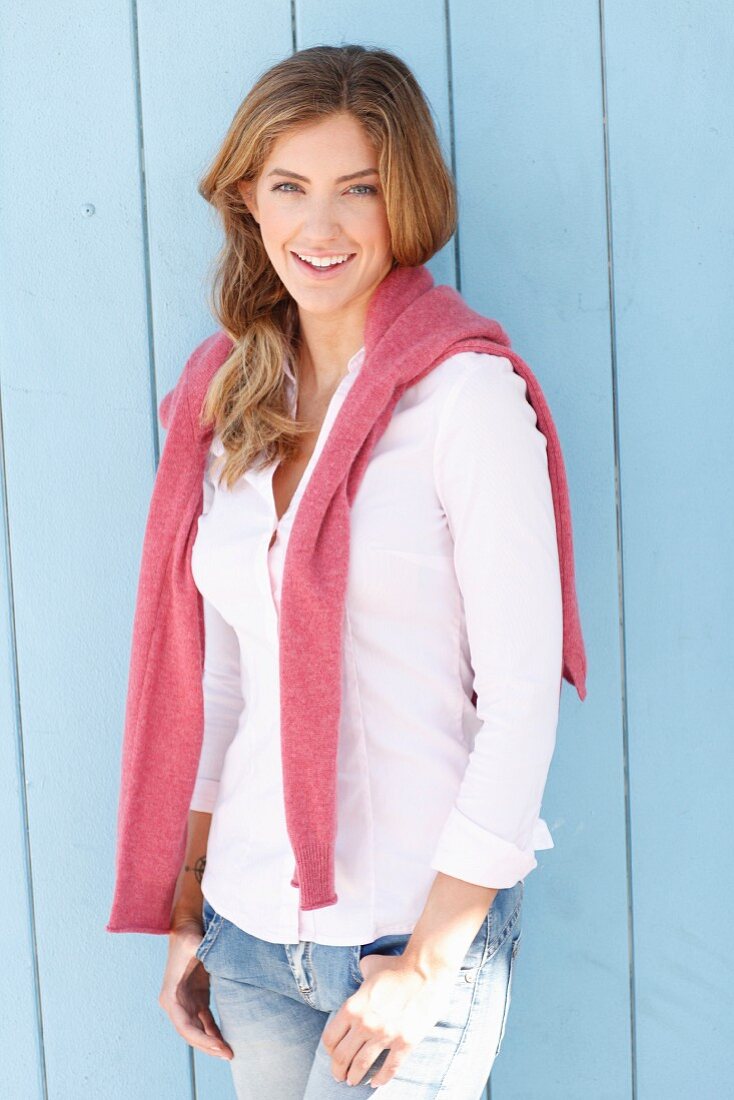 A young woman wearing a white blouse, a pink jumper draped around her shoulders and jeans