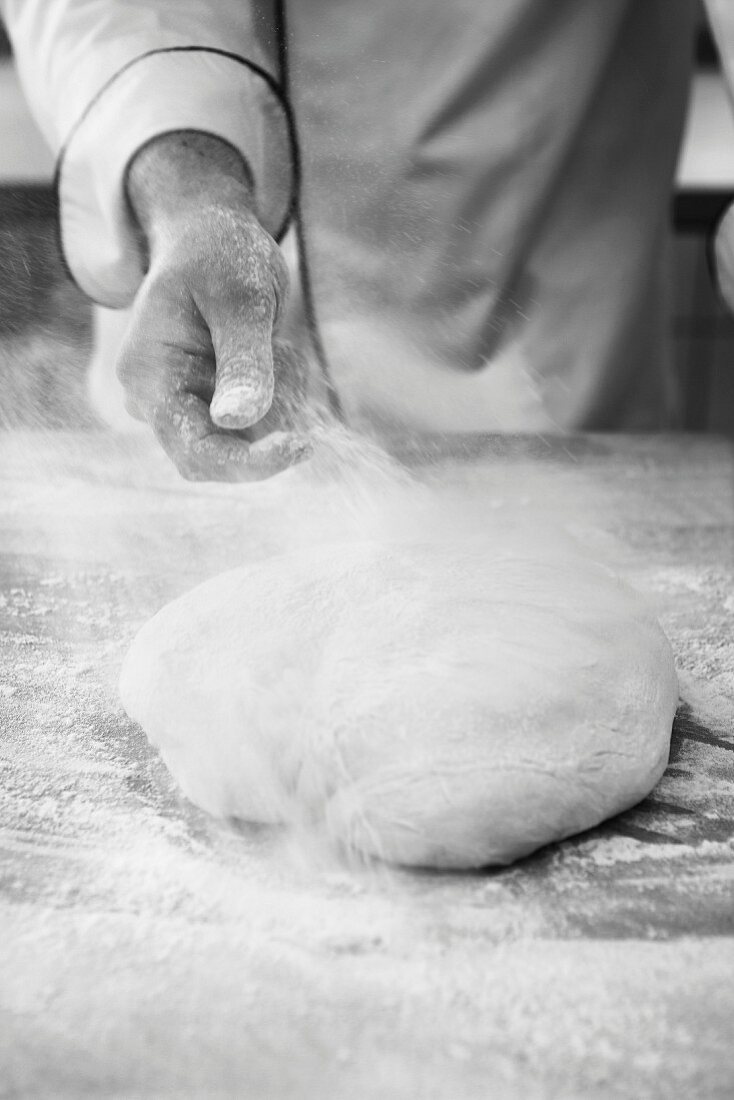A baker dusting bread dough with flour