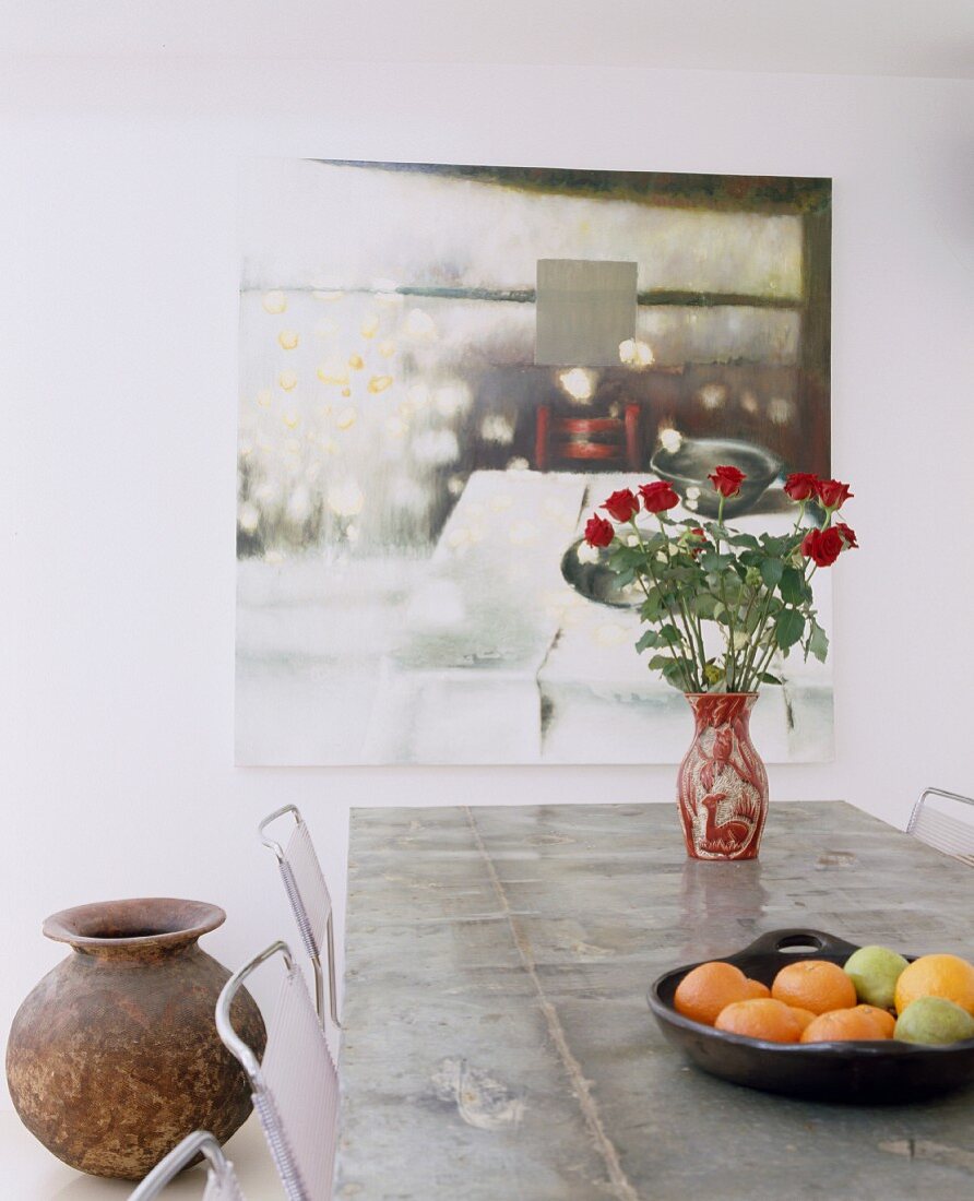 Vase of red roses on table in front of painting