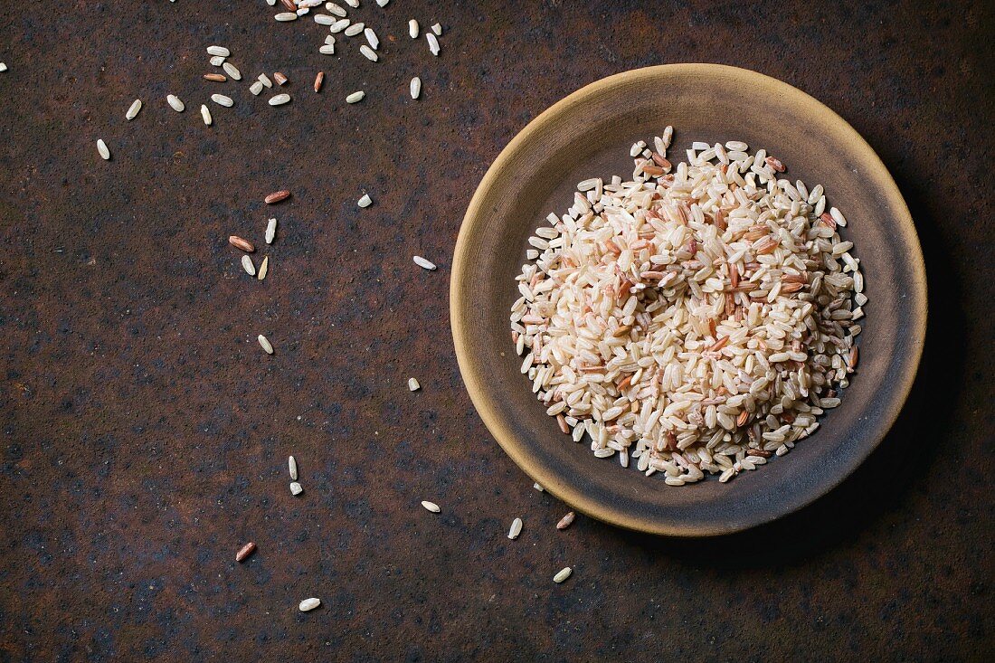 Ungekochter brauner Reis auf Teller vor braunem Hintergrund