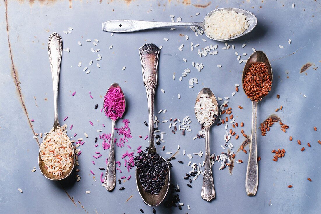 Set of unusual rice in vintage spoons over gray metal surface